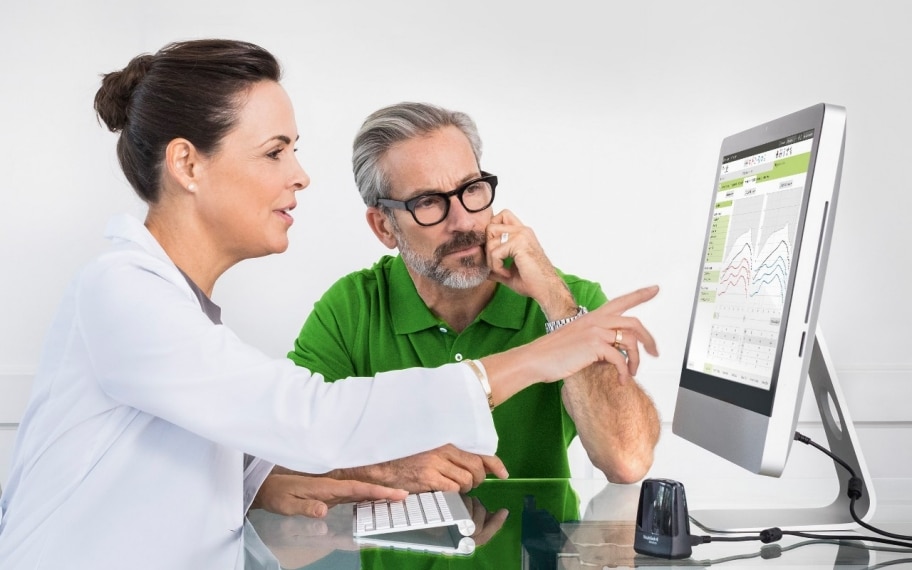 Audioprothésiste s’adressant à un patient devant un écran.