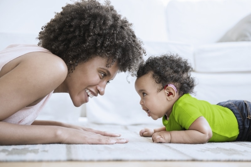 Mother playing face to face with baby son on floor