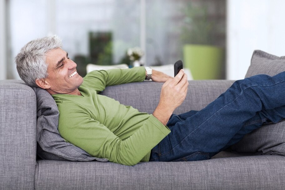 middle aged man reading text message on mobile phone while lying on couch